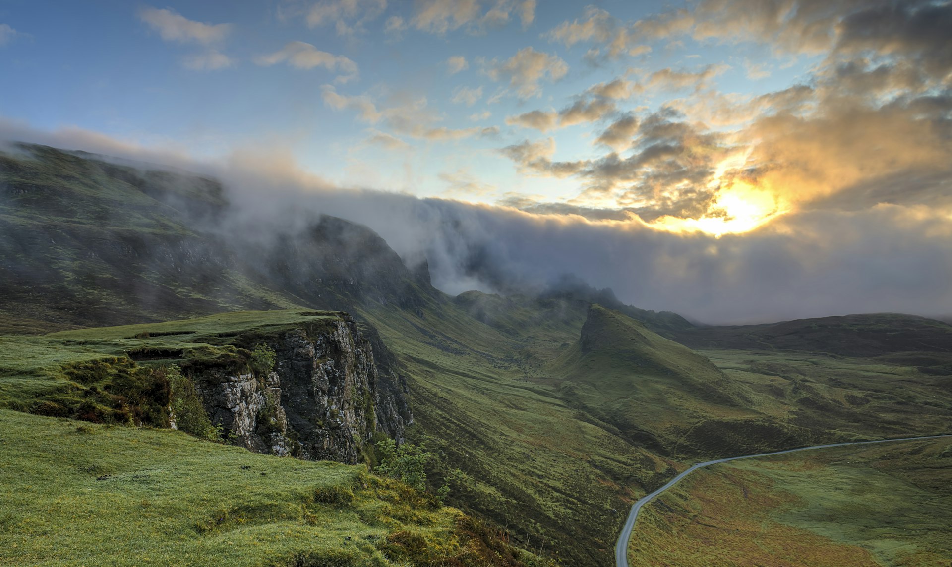 Sunrise breaking over a misty green hillside path